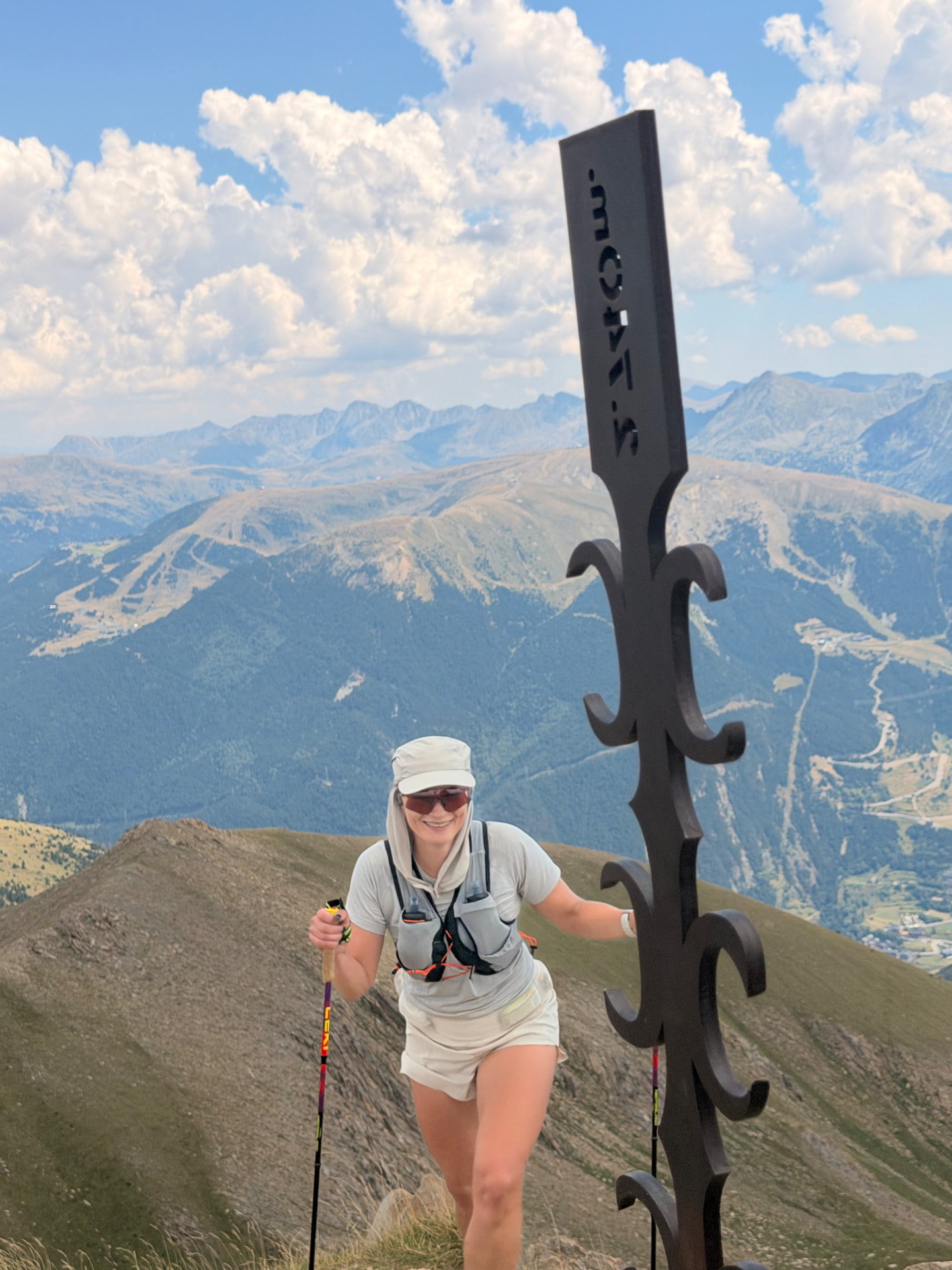 Trail runner with poles reaching a Pyrenees summit signpost above Ordino