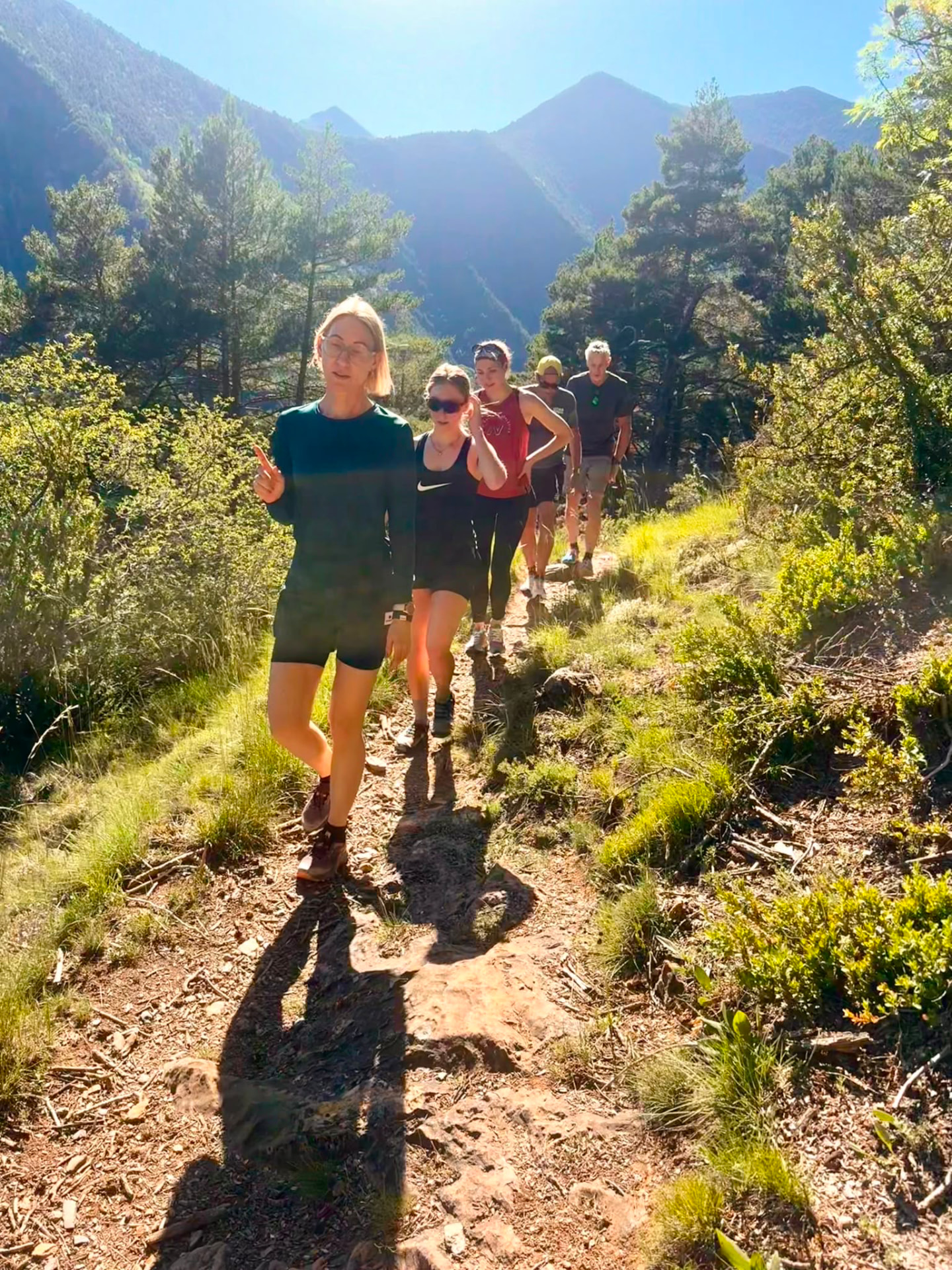 Runners climbing single file on a sunlit trail with Pyrenean peaks behind