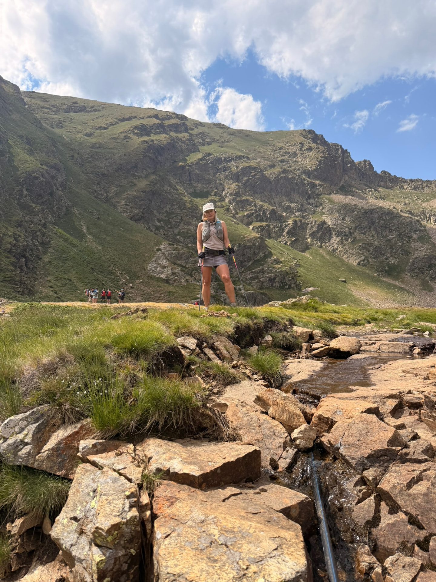 Runner with poles above a mountain stream on the Coronallacs route
